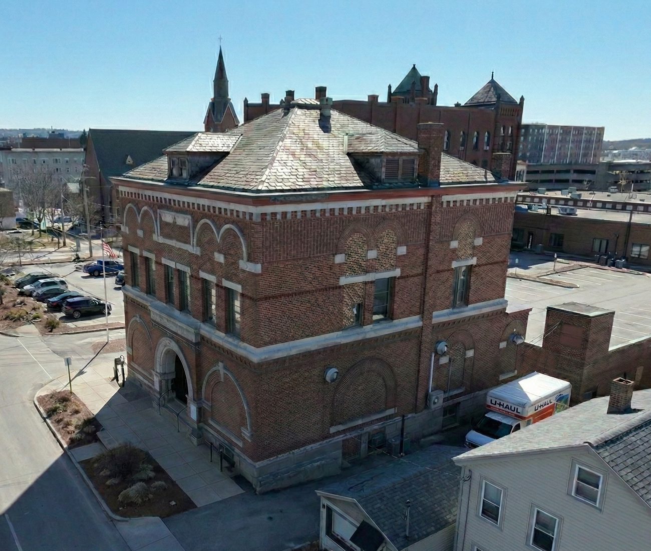 Aerial oblique of a historic brick building with a slate hip roof and its parking lot