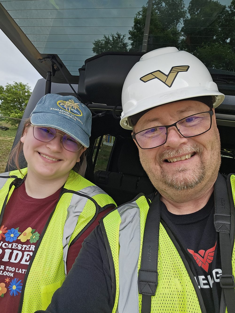Two members of the Osprey Drone Solutions crew in high-visibility vests and a hard hat, seated in a utility vehicle on site