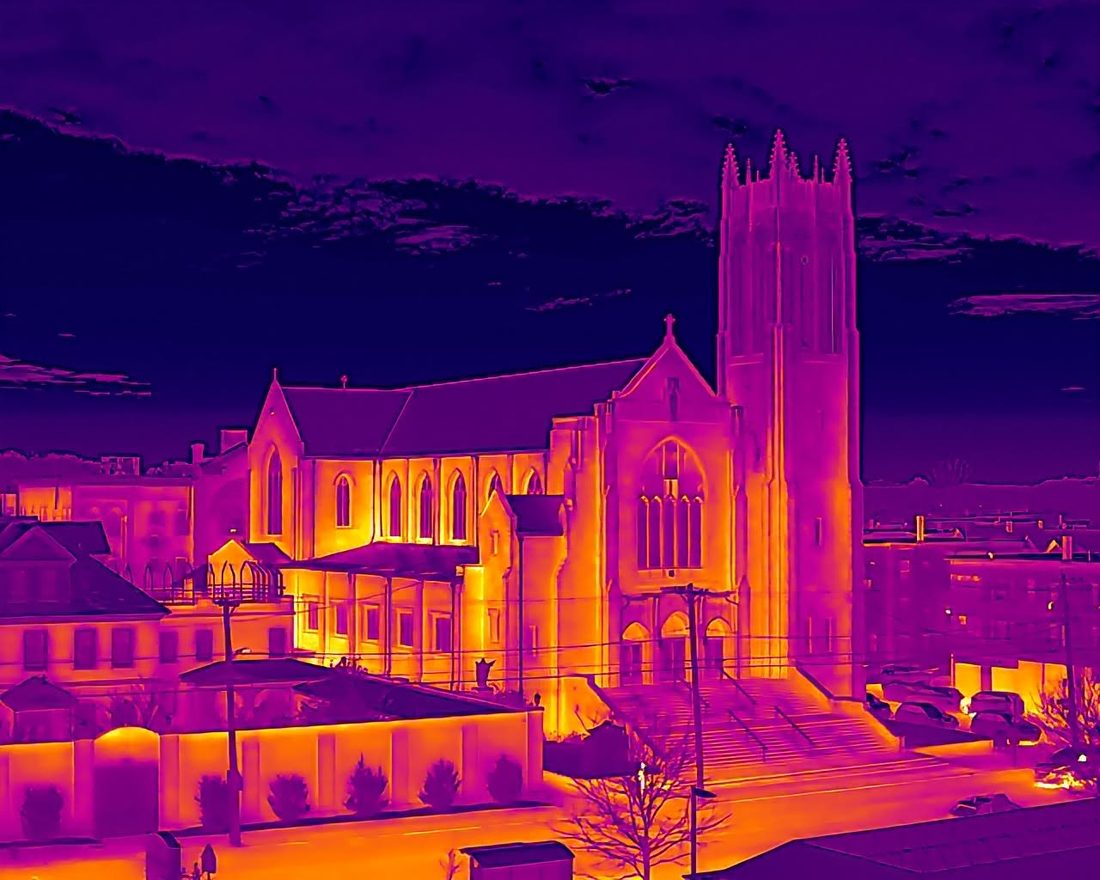 Thermal image of a stone church and bell tower at dusk, walls glowing orange against a purple sky